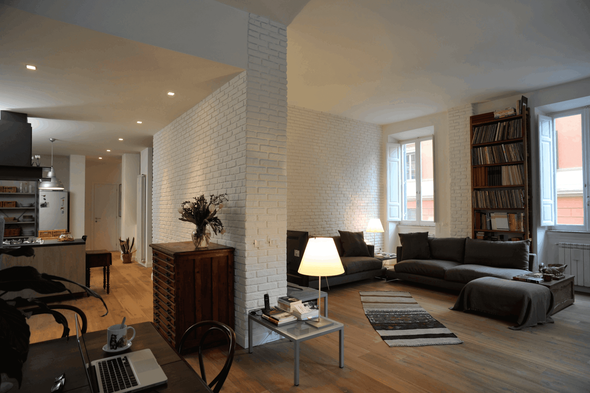 Modern living room with white brick walls, sofas, a wooden cabinet, and a table lamp.
