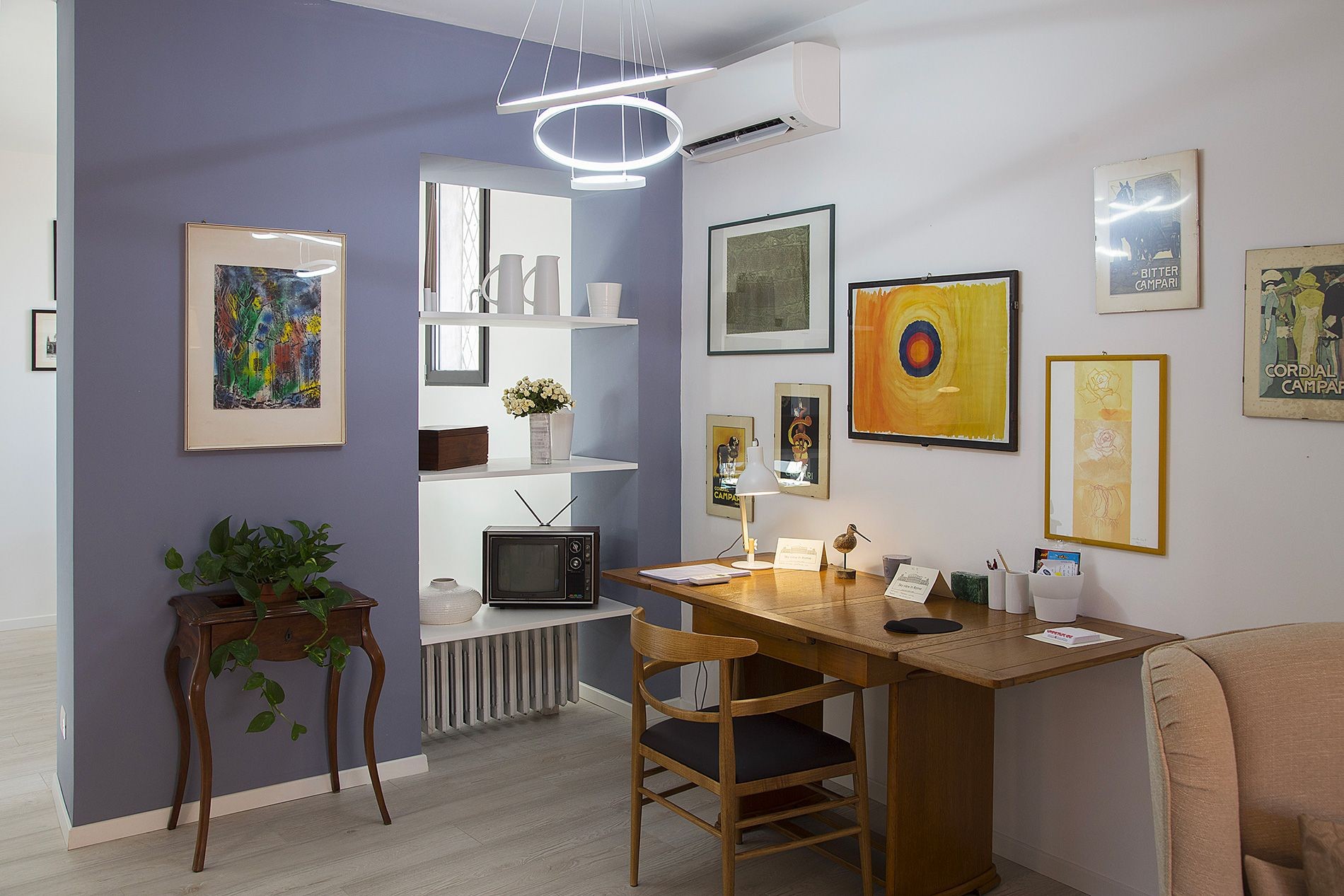 Cozy home office with wooden desk, plant, shelves, and artwork on light blue walls.